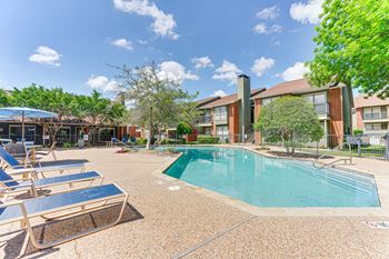 A swimming pool surrounded by sun loungers and trees.